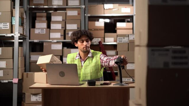 Man in safety vest scanning the barcode of shipment at his workplace in warehouse. Arabic worker working in a drop-shipping office, preparing a parcel to deliver