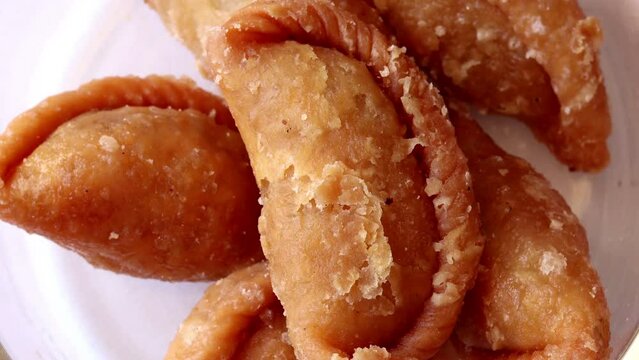 Indian festival sweet Gujiya or Gujia on small bowl isolated on white background. Table top spin view