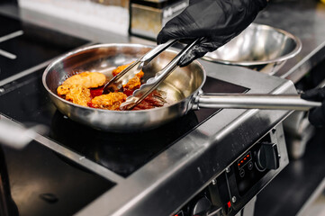 woman chef cooking chicken wings in a sauce in the kitchen