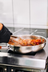 woman chef cooking chicken wings in a sauce in the kitchen