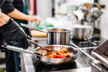 woman chef cooking chicken wings in a sauce in the kitchen