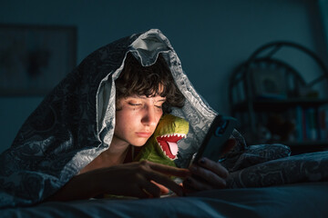 portrait teenage girl sitting under covers on bed, using phone
