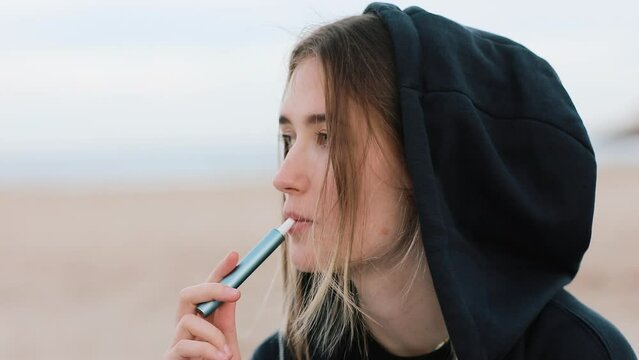Electronic cigarette technology. Young woman smokes and releases steam from hybrid cigarette device that uses real tobacco refills with a heating pad, tobacco heating system. Bad unhealthy habit.