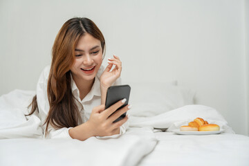 Happy young woman asian using mobile phone lying on the bed at home