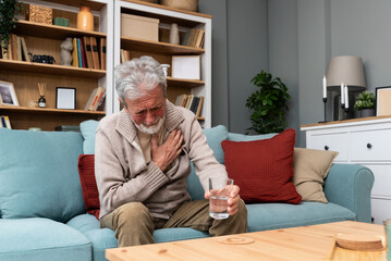 Senior older man getting chest pain in living room, heart attack holding his hand on the chest...
