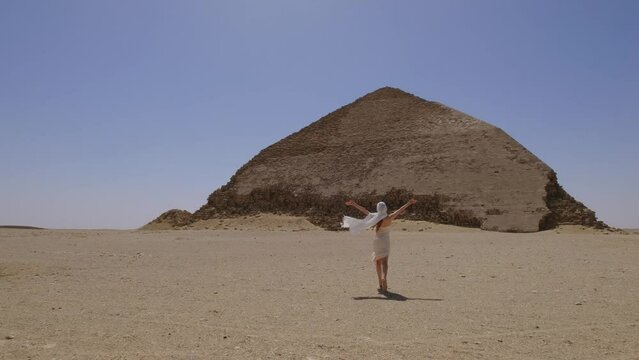Woman in a white dress is running. On the background is The Red Pyramid.