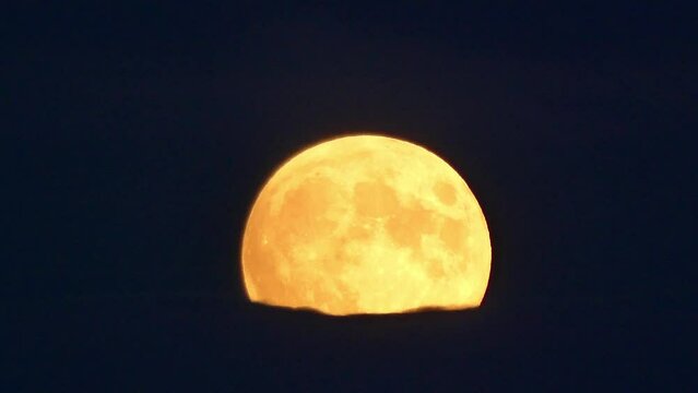 Dark night sky, orange moon during rising and moving dark clouds. Moon disc in close-up with visible craters - accelerated pace. Topics: weather, cosmos, toposphere, night time