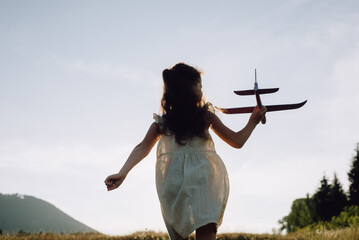 Silhouette of little girl kid run with airplane on background amazing mountains during warm summer...