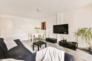 a living room with white walls and wood flooring, black couches and a flat screen tv on the wall