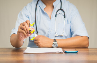 Physician ticks the correct sign with yellow marks in checkboxes while sitting at the table in the hospital.