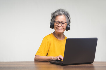 Cheerful senior woman wearing wireless headphones with a smile while sitting at the table.