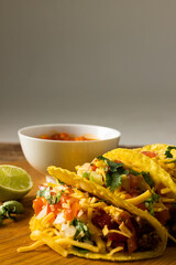 Close-up of tacos filled with cheese, meat and vegetables on wooden table against gray background