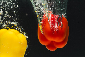 Close up of peppers falling into water with copy space on black background