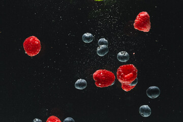 Close up of fresh berries falling into water with copy space on black background