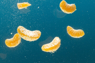 Close up of tangerine segments falling into water with copy space on blue background