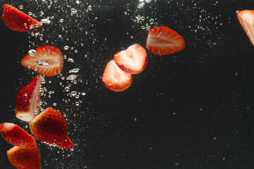 Fototapeta premium Close up of strawberries falling into water with copy space on black background