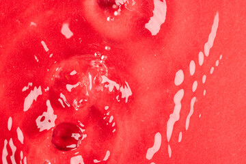 Close up of water drop falling into water with ripples and copy space on red background