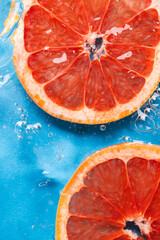 Close up of red grapefruit slices in water with copy space on blue background