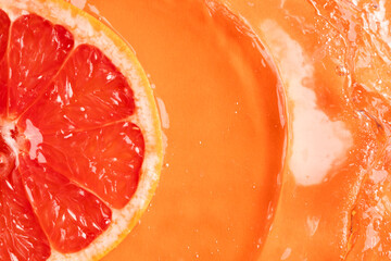 Close up of red grapefruit slice in water with copy space on orange background