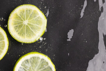 Close up of lime and lemon slices in water with copy space on black background