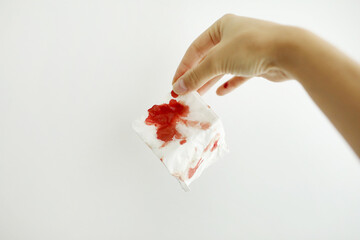 Female hand holds and shows paper tissue with blood stain in light room. Bleeding wound, body...