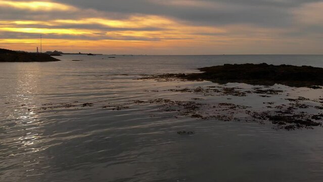 Aerial Drone shot slowly pushing out over the sea into St Aubin's Bay at sunset in Jersey, Channel Islands.