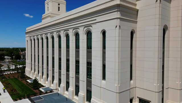 Drone flying around Layton Temple that is in construction close up seeing construction workers walking around and taking break from hot summer sun, blue sky and Wasatch mountain range in background.