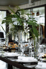 Luxuriously set wedding table, vases with white flowers and fern leaves on the table, food and drinks. Side view.