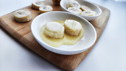Sliced round Pieces of Banana on white plate and on wooden board on white background. Banana cooking, Close up. Delicious sweet fruit dessert