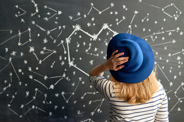 Rear view of female astrologer looking at blackboard with pictured constellation of stars in shape...