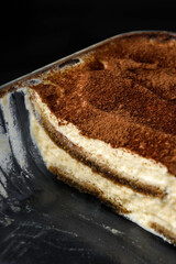 Homemade tiramisu cake in glass baking dish on black background.