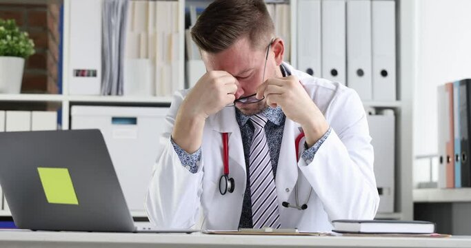 Tired doctor sitting at computer and taking off his glasses 4k movie. Medical error concept