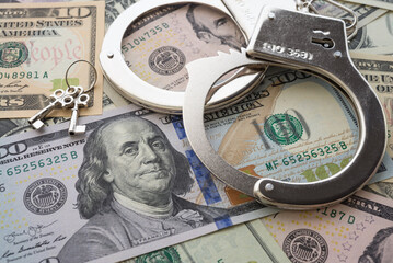 Pair of metal police handcuffs on USD US dollar banknotes money cash background.  Corruption, dirty money, gambling or financial crime ideas concept.