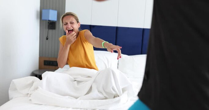 Woman sitting in bed and laughing at man standing in front of her 4k movie. Problems with male potency concept