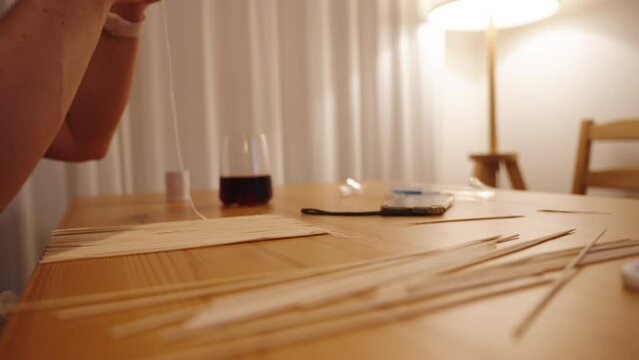 A woman is making a mat for rolling sushi using wooden skewers.