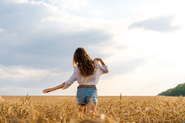 a beautiful young woman stands in a field of wheat with developing hair in the wind against the sky