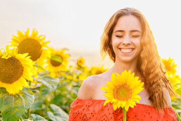 happy smiling woman in a red dress at sunset in a field of sunflowers, holding a flower in her hand,