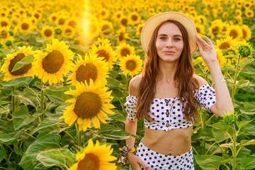 beautiful young woman in a straw hat at sunset posing in a field of sunflowers, against the sky