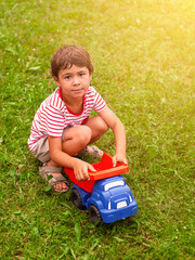 A little boy is playing with a toy car on the green grass.