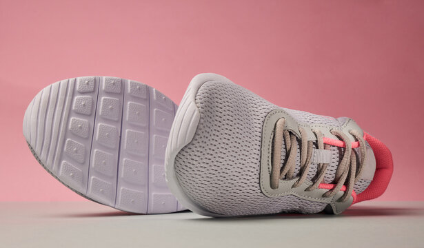 Gray and pink running shoes laying on the side on a gray surface with a pink background