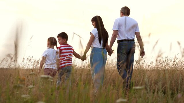 Happy family with adorable little children walks across field at sunset light