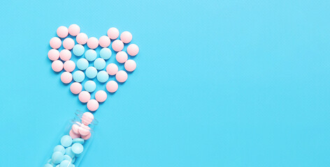 Glass bottle with pink and blue pills. Heart lined with vitamins on a blue background, top view. Healthcare, medical pills and dietary supplements. Pharmaceutical medicines