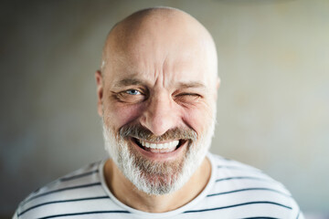 Portrait of excited emotional bald mature man with gray beard and mustache laughing cheerfully and...