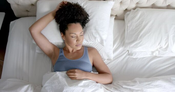 Overhead view of biracial woman sleeping in bed in bedroom, slow motion