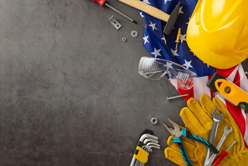 Honoring contribution of construction workers on American Labor Day. Above view photo of flag, helmet, gloves and building tools on grunge textured grey concrete background with copyspace