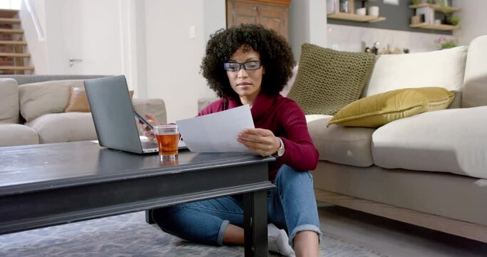 Happy biracial woman using laptop and smartphone at home, slow motion
