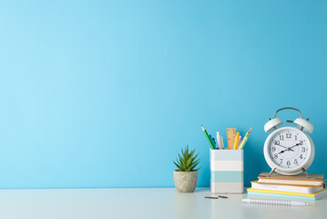 Promote a productive study environment with side-angle photo featuring white desk, alarm clock, notepads, penholder, and office supplies on blue backdrop, providing ample copy-space for text or ads