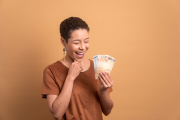 happy black young woman looking at brazilian money cash in beige colors. economy, credit, payment,...