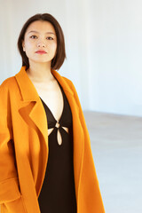 Portrait of a young Chinese woman wearing a nice orange coat and a black skintight dress.
