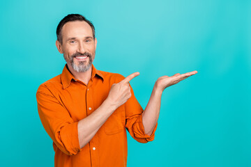 Photo of confident positive man dressed orange shirt showing finger holding arm empty space...